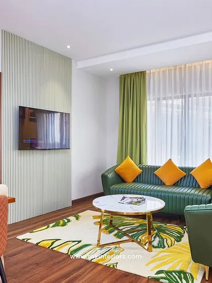 This hotel suite's living area is designed for comfort and style. The space features a vibrant green sofa, a patterned rug, and a copper pendant light, creating a modern and inviting atmosphere for guests to relax or work.