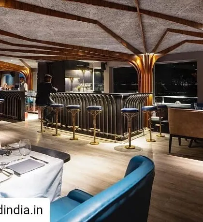 The restaurant's interior bar and dining area at night. The lighting design was critical, using concealed sources and warm tones to create an intimate and inviting atmosphere that contrasts with the dark water and bright city lights outside.