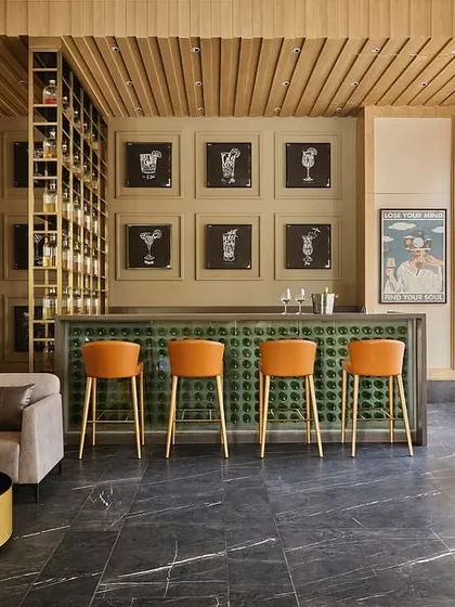 The custom-designed bar at Rustomjee Elements features a unique counter front made of green glass bottles, quirky chalkboard-style graphics, and comfortable, modern bar stools.