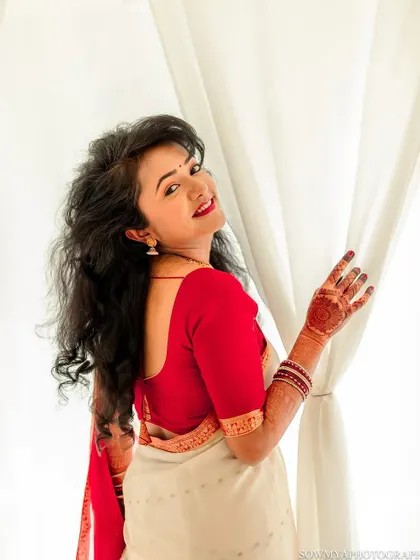 A bright and happy bridal portrait. The bride looks back with a radiant smile, her hair and saree gently lit by the window light.