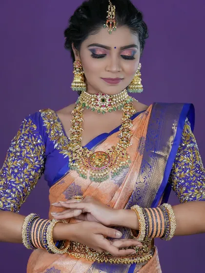 A detailed look at a bridal set featuring a choker and a longer necklace with green and ruby-colored stones, paired with a matching vaddanam.