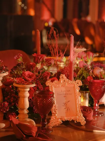 A table detail showing an ornate gold frame, red goblets, and candles, creating a rich and opulent vignette.