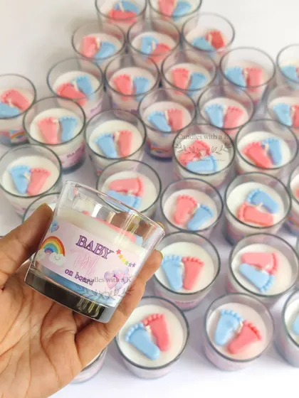 A close-up of a personalized baby feet candle, highlighting the custom sticker and the delicate details of the pink and blue wax feet.