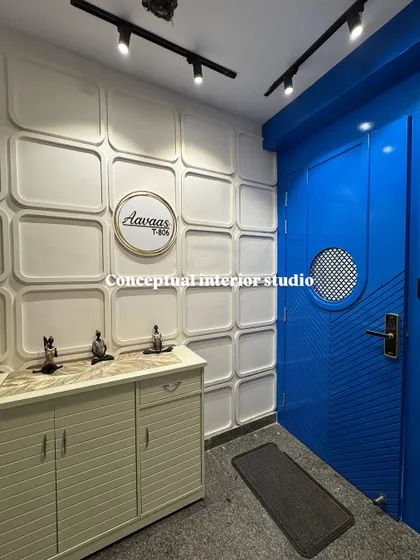 A bold and beautiful foyer in a 4BHK. The vibrant blue door contrasts perfectly with the white 3D wall panels and the simple shoe cabinet.