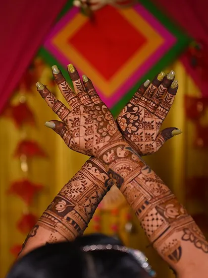 A creative shot of a bride's hands, showcasing the intricate mehendi design against a festive backdrop.