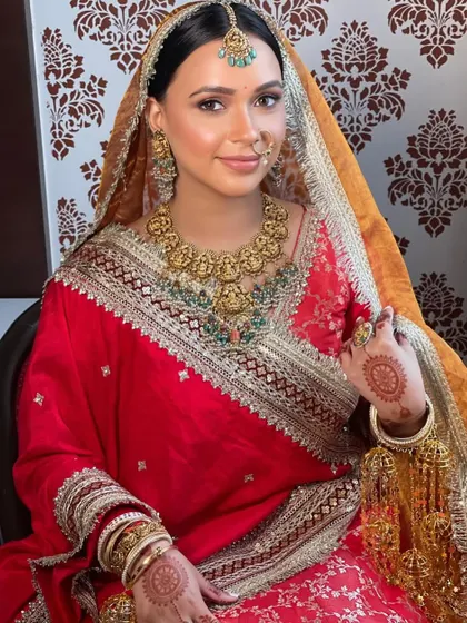 A royal bride in red and gold. Her hair is styled in a clean, elegant bun to complement her majestic look.