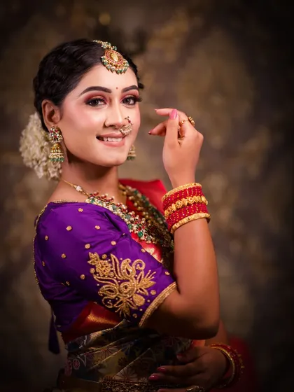 A happy and candid shot. The makeup is fresh and vibrant, with a pop of color on the lips that matches the red in her saree.
