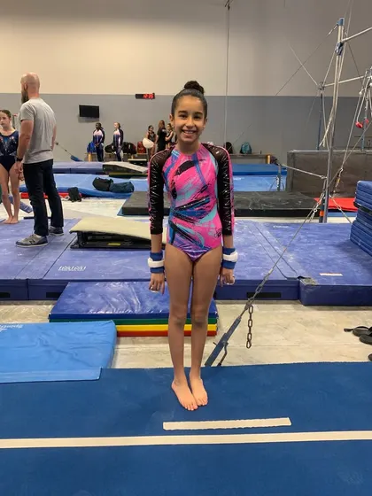 An Xcel Gold gymnast stands ready by the bars, showcasing the focus required for competitive gymnastics.