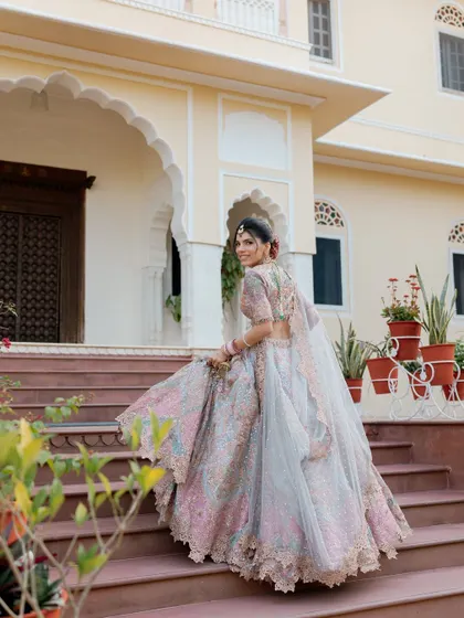 A classic bridal shot, with the bride looking back with a smile as she ascends the steps of a beautiful palace, her pastel lehenga flowing behind her.