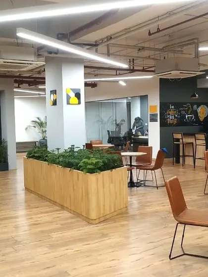 A wide view of the central breakout space at VentureX Gurugram. This area combines a cafe, lounge seating, and planters, serving as the energetic heart of the coworking office.