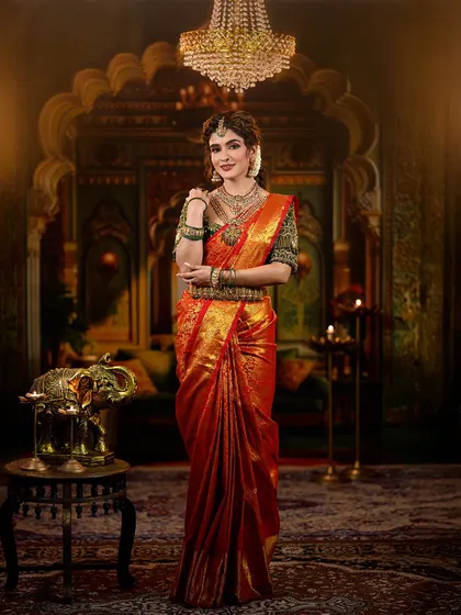 A regal and traditional bridal look featuring a rich red and green Kanjivaram saree. The makeup is defined by warm, shimmery eyes and a deep red lip, perfectly accessorized with temple jewelry.