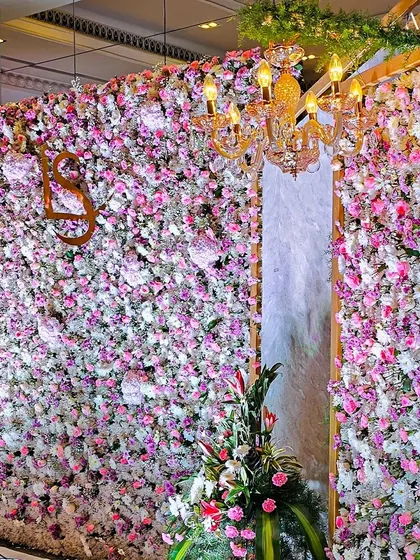 The golden chandelier adds a touch of luxury to the lush floral wall, creating a beautiful contrast between the soft petals and the warm metallic glow.