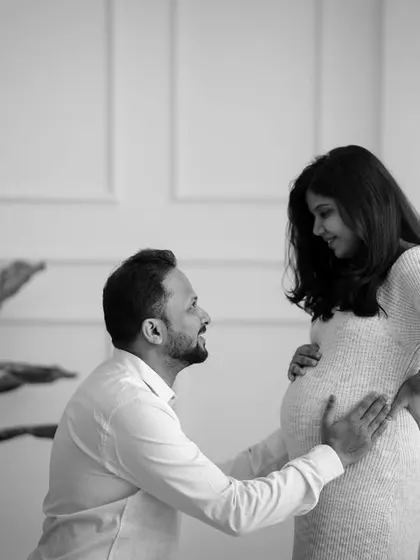 A tender moment between parents-to-be, captured in timeless black and white. The father-to-be kneels, looking up lovingly at his partner.