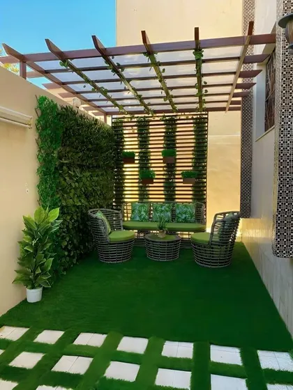 A modern patio design with artificial turf, a comfortable seating area, and a pergola for shade. The vertical garden wall adds a lush green backdrop.