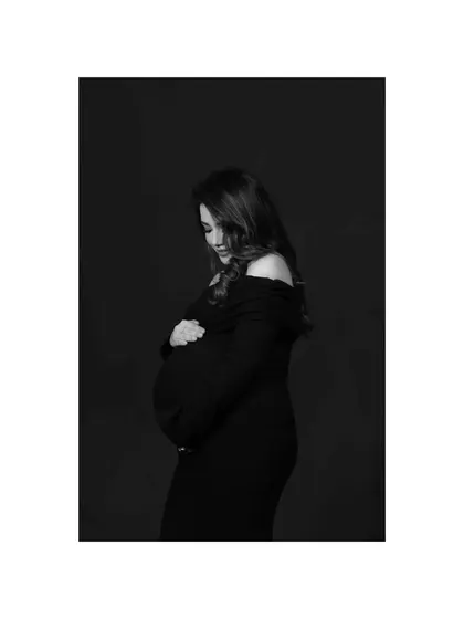 A contemplative black and white portrait. The mother-to-be cradles her bump, her expression soft and thoughtful, in this beautifully lit, low-key studio shot.