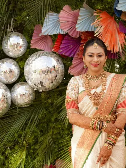 Bride Deekshitha against a festive backdrop. Her custom puff-sleeve blouse with red detailing is a perfect match for her traditional wedding saree.