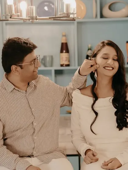 A playful and sweet moment in a kitchen-themed studio set, with the groom-to-be gently pinching his partner's cheek.