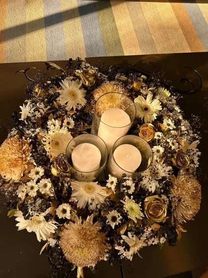 A floral centerpiece designed for an intimate home party. This arrangement uses a sophisticated palette of white, black, and gold-sprayed flowers, with pillar candles in the center for a warm glow.