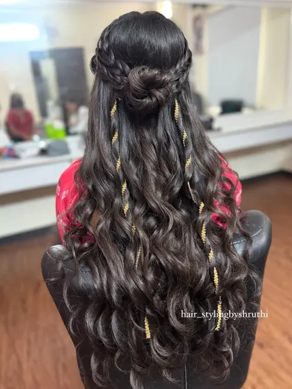 This half-up style features a braided crown, a small bun, and loose waves accented with delicate golden leaf accessories. The gold details add a touch of warmth and elegance.