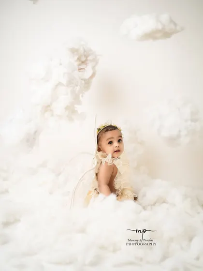 An angel peeking out from behind the clouds. The all-white theme creates a pure and serene atmosphere for these beautiful milestone photos.