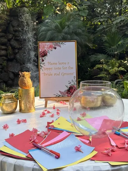 A guest wish station set up by a waterfall, where guests can leave colorful notes for the bride and groom in a large glass bowl.
