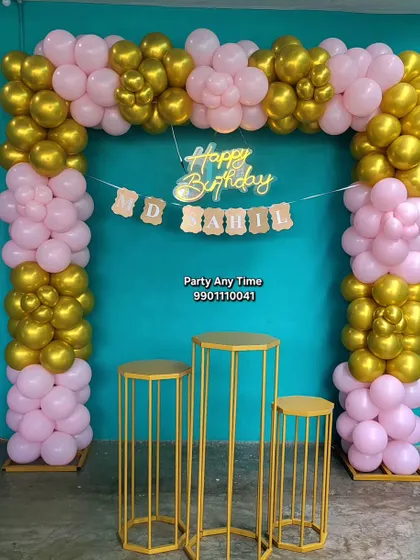 A simple pink and gold balloon arch against a teal wall, perfect for home parties in Kanakapura.