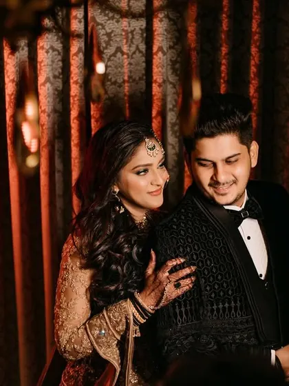 A candid moment of affection, with the bride gently resting her hand on her groom's shoulder. The warm, textured background and their relaxed expressions make this a beautiful, natural portrait.