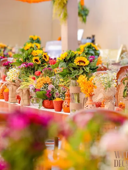 A close-up of the tablescape, featuring a vibrant mix of sunflowers, marigolds, and other seasonal blooms in terracotta pots and burlap-wrapped vases. Every detail was chosen to enhance the rustic, earthy feel.