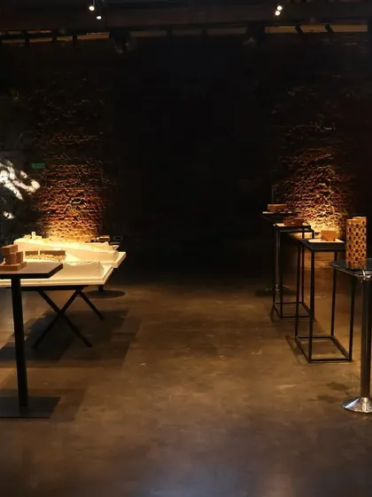An empty exhibition hall at IF.BE, with models spotlit against the dark, textured walls. The atmosphere of the space itself, with its history and character, plays a crucial role in how the work is perceived.