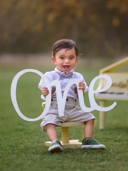 Celebrating one whole year of smiles. This outdoor first birthday portrait captures the excitement of the milestone, with props like the "One" sign and a mini piano adding a touch of charm.