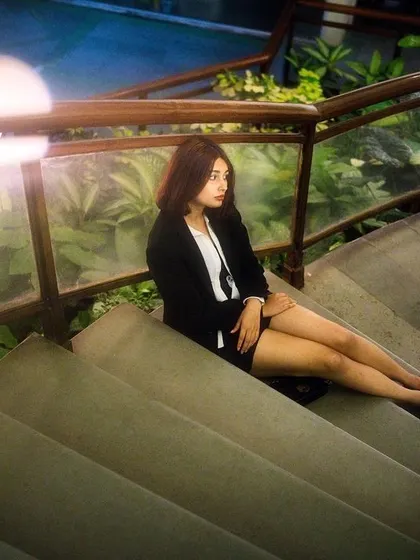 A pensive portrait of a woman sitting on a concrete staircase at night. The soft lighting and quiet setting evoke a sense of thoughtful solitude in an urban environment.