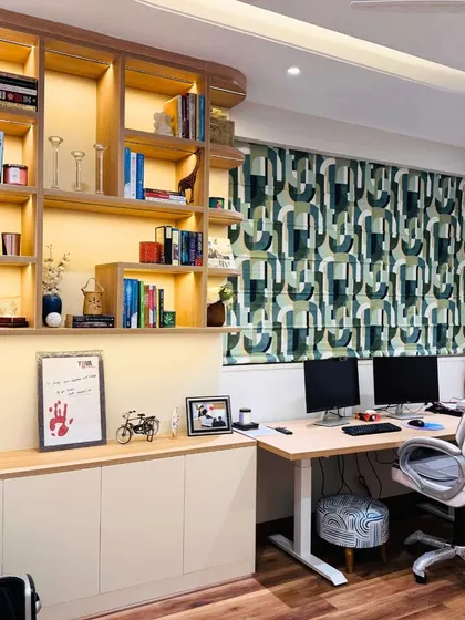 A well-organized and stylish home office with extensive backlit shelving for books and decor, a spacious desk for two, and vibrant patterned curtains.