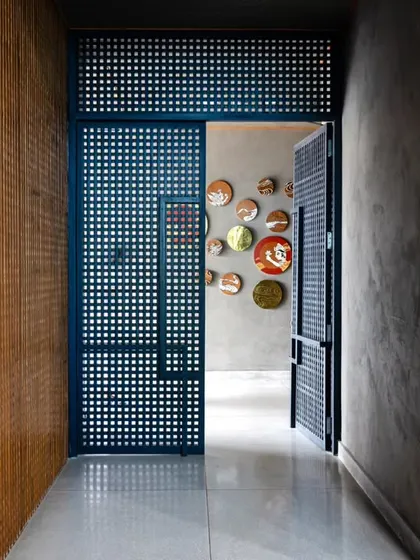 The entrance to the guest lounge, framed by teakwood blockwork and the striking blue door. The design uses a consistent language of raw materials and thoughtful details to guide visitors through the space.