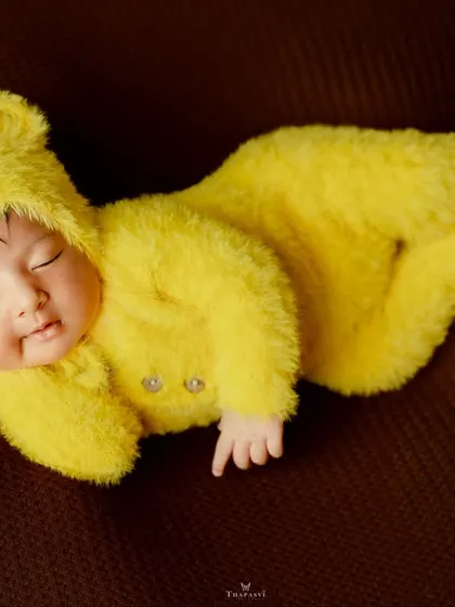 A simple, beautiful shot of a newborn in a fuzzy yellow bear costume, curled up and sleeping soundly on a rich brown background.