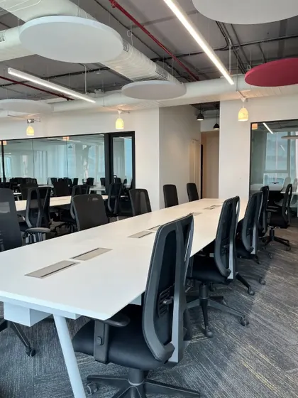 An expansive view of the Kissflow office, showing a long conference table integrated within the open workspace. The exposed ceiling and ductwork give the space an industrial feel, which is softened by the large, nature-inspired wall mural.