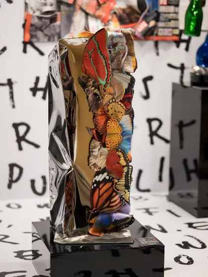 'Wings of Reflection' is a sculpture that combines industrial texture with the delicate beauty of butterflies. The crumpled metallic form adorned with colorful wings creates a striking contrast, representing transformation and resilience.
