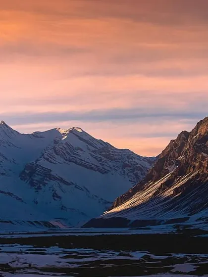 The soft pink and orange hues of a winter sunset over the Spiti mountain range. The light hits the snow-capped peaks in a way that's just pure magic.