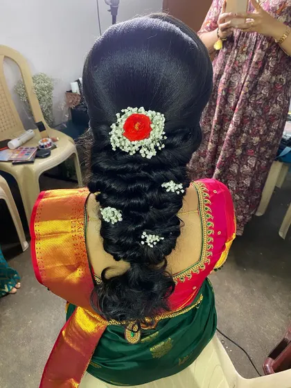 A lovely messy braid with a high puff, decorated with baby's breath and a bright red flower. This hairstyle is perfect for an engagement or pre-wedding celebration.