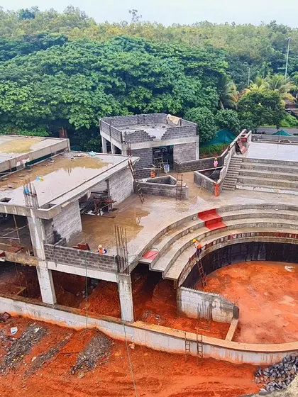 An aerial view of the TAPMI Centre's concrete structure during construction, highlighting the building's footprint and its relationship to the surrounding green campus.