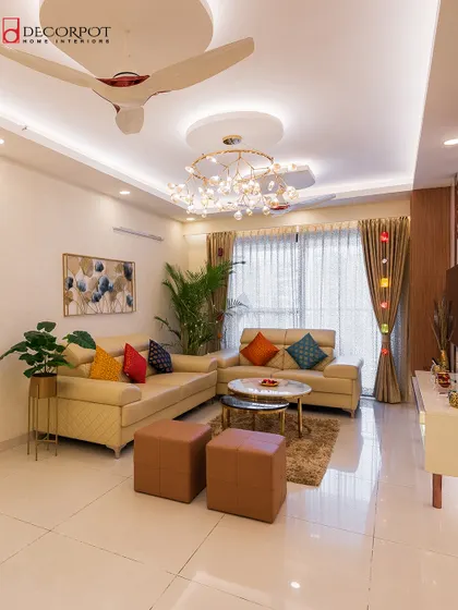 We designed this living room to be a vibrant and welcoming space. A neutral-toned sofa is brought to life with colorful cushions, complemented by a modern chandelier and a functional TV unit.