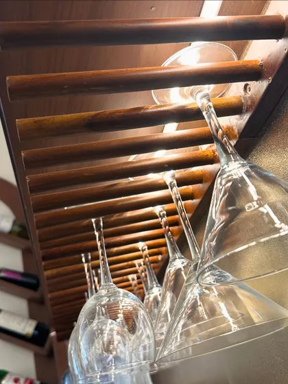 A close-up of a custom-built wooden glass rack in a home bar. This simple, slatted design is both a practical storage solution and a beautiful detail that enhances the overall aesthetic.