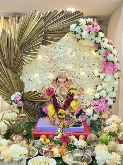 This modern Ganpati decor combines traditional flowers with contemporary elements. A beautiful crescent of white and pink flowers is accented with large, golden dried palm leaves, creating a stylish and sophisticated look for the festival.