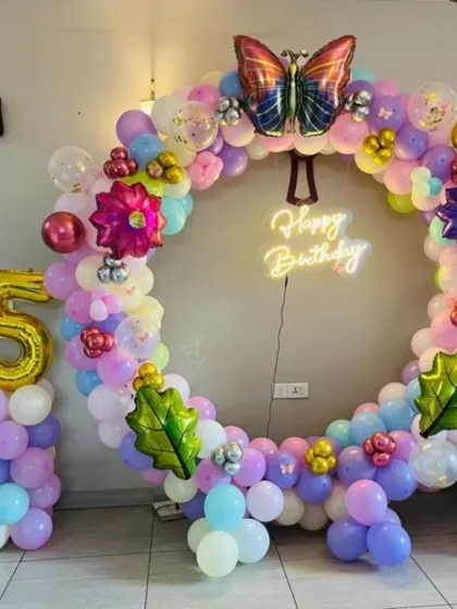 A colorful butterfly-themed 5th birthday party. This decoration features a circular balloon arch, a "Happy Birthday" neon sign, and a large number '5' foil balloon.