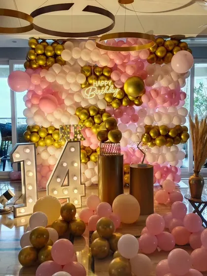 A pink and gold themed 14th birthday party with a full balloon wall and marquee numbers.