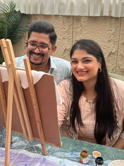 A couple shares a smile while working on a painting at their baby shower. My art parties are all about creating joyful memories together.