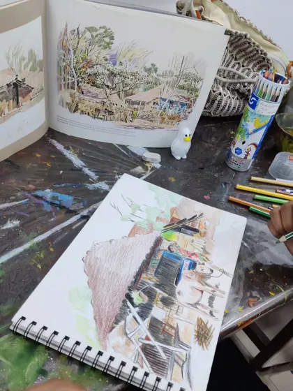 The student's workspace, showing her drawing in progress alongside the reference image from an art book.