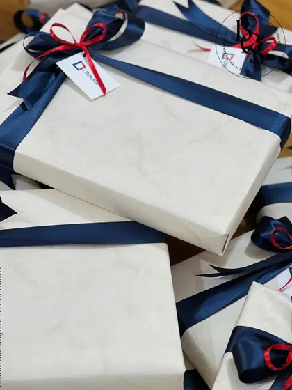 A corporate gift order for Unilight. The presents are wrapped in a subtle white marble-patterned paper and secured with a navy blue satin ribbon, featuring a custom tag with the company's logo.