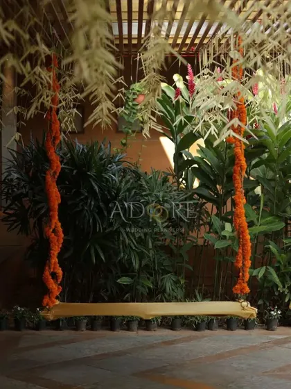 An 'unjal' (swing) decorated with marigold garlands, set against a lush green background. This traditional element provides a beautiful and symbolic spot for wedding rituals and photos.