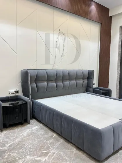 This elegant grey velvet bed features a tufted, winged headboard and a matching upholstered frame. It is paired with a unique fluted bedside table with a black glass top, combining classic comfort with modern details.