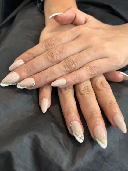 A modern twist on a timeless classic. These almond-shaped nail extensions feature a clean French manicure, elevated with a delicate gold line and a few sparkling rhinestones for a touch of elegance.